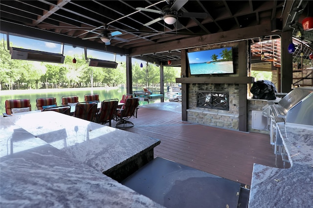 wooden terrace with an outdoor stone fireplace, area for grilling, and ceiling fan