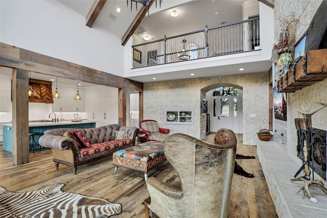 living room with beam ceiling, sink, light hardwood / wood-style flooring, and high vaulted ceiling