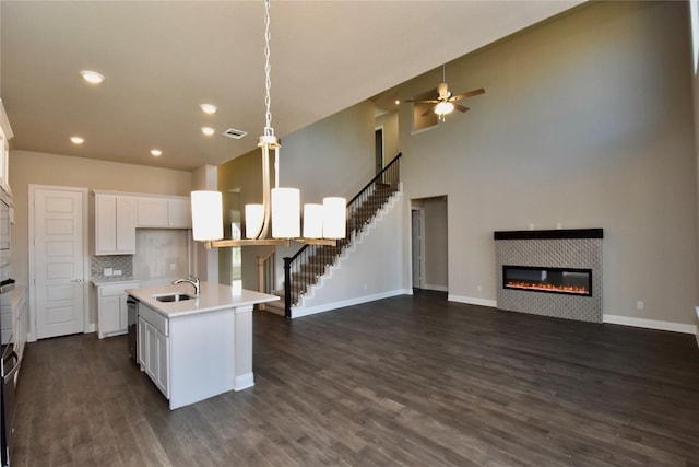 kitchen with a tile fireplace, white cabinets, hanging light fixtures, sink, and an island with sink