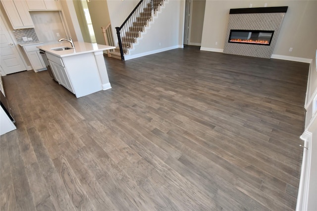 kitchen featuring backsplash, dark wood-type flooring, a tile fireplace, white cabinets, and an island with sink