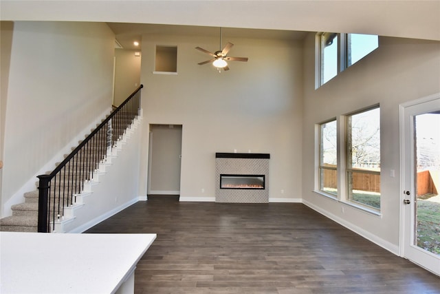 unfurnished living room featuring a tiled fireplace, ceiling fan, dark hardwood / wood-style flooring, and a high ceiling