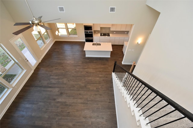 unfurnished living room with ceiling fan, dark wood-type flooring, and a high ceiling