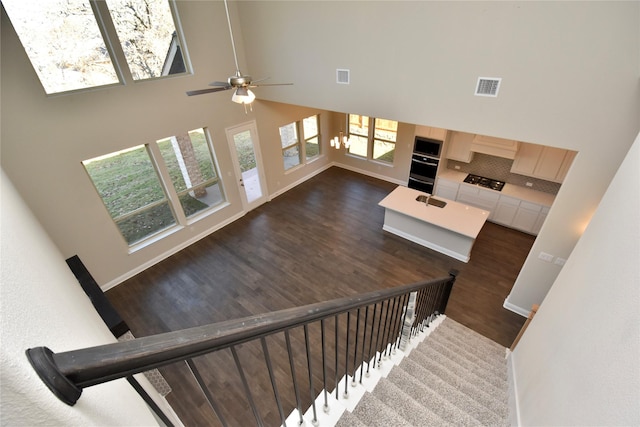 stairs with ceiling fan with notable chandelier, a high ceiling, and hardwood / wood-style flooring