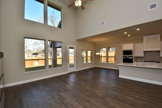 unfurnished living room featuring a high ceiling, ceiling fan with notable chandelier, dark hardwood / wood-style flooring, and sink