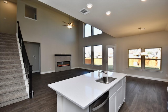 kitchen featuring white cabinets, dishwashing machine, an island with sink, and decorative light fixtures