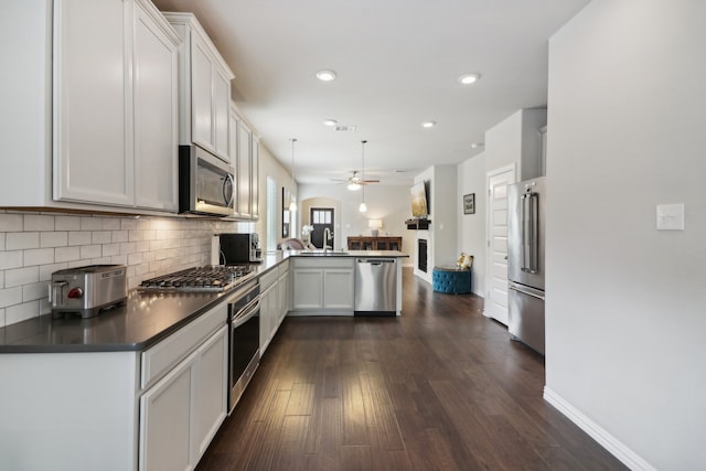 kitchen featuring kitchen peninsula, white cabinets, appliances with stainless steel finishes, dark wood-type flooring, and sink