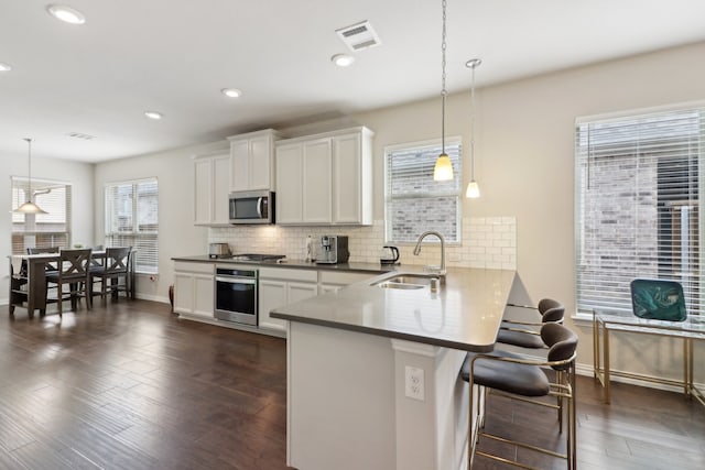 kitchen featuring kitchen peninsula, stainless steel appliances, sink, a breakfast bar, and decorative light fixtures