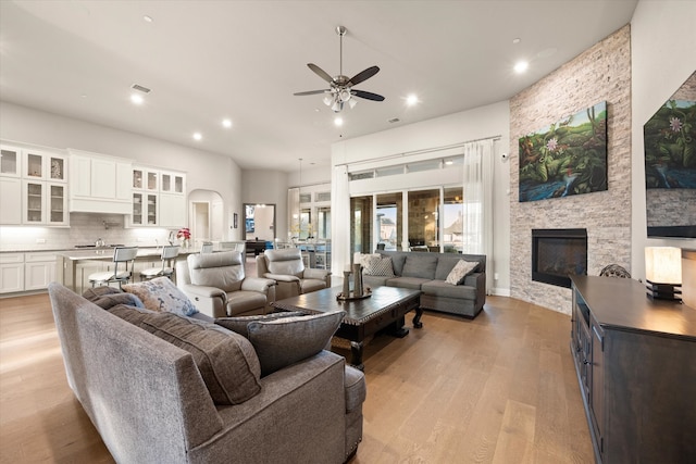 living room with sink, a stone fireplace, light hardwood / wood-style floors, and ceiling fan