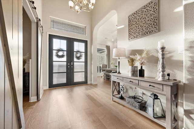 entrance foyer featuring light hardwood / wood-style floors, french doors, a barn door, and an inviting chandelier