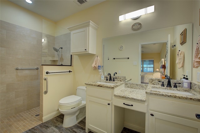 bathroom featuring toilet, hardwood / wood-style flooring, vanity, and a tile shower