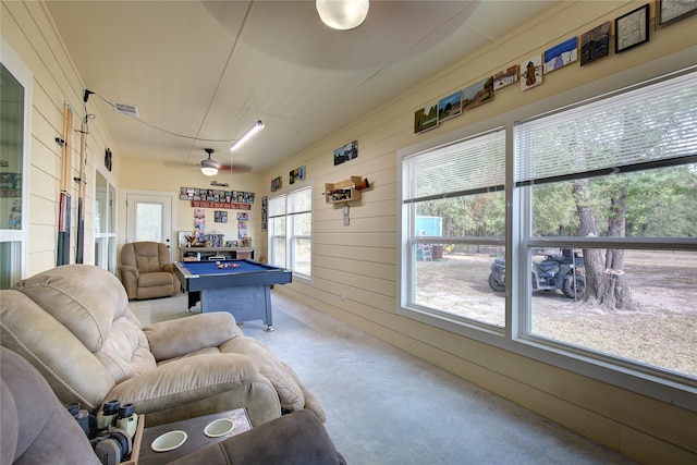 recreation room featuring concrete flooring, a healthy amount of sunlight, pool table, and wood walls