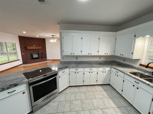 kitchen with sink, electric range, a brick fireplace, and white cabinets