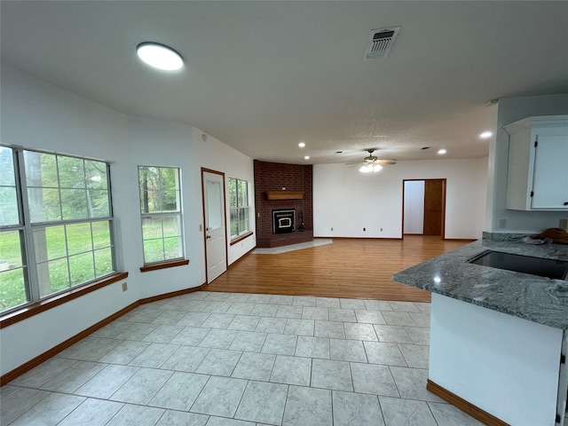 unfurnished living room featuring a fireplace, a healthy amount of sunlight, light wood-type flooring, and ceiling fan