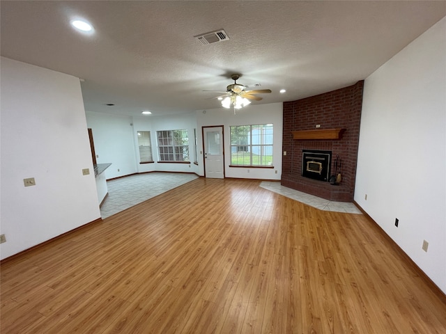 unfurnished living room with a brick fireplace, a textured ceiling, light wood-type flooring, and ceiling fan