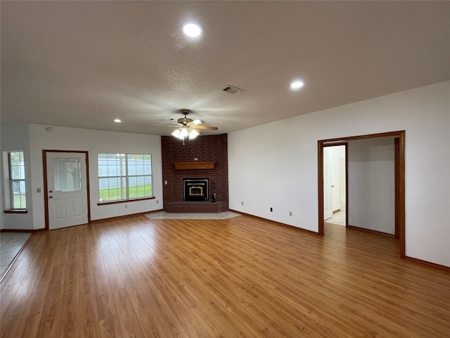 unfurnished living room featuring light hardwood / wood-style flooring, ceiling fan, a brick fireplace, and a wealth of natural light