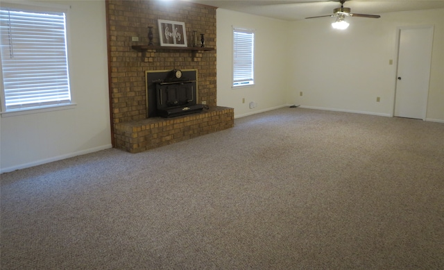 unfurnished living room with a wood stove, carpet floors, and ceiling fan