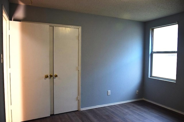 unfurnished bedroom featuring a textured ceiling, a closet, and dark wood-type flooring