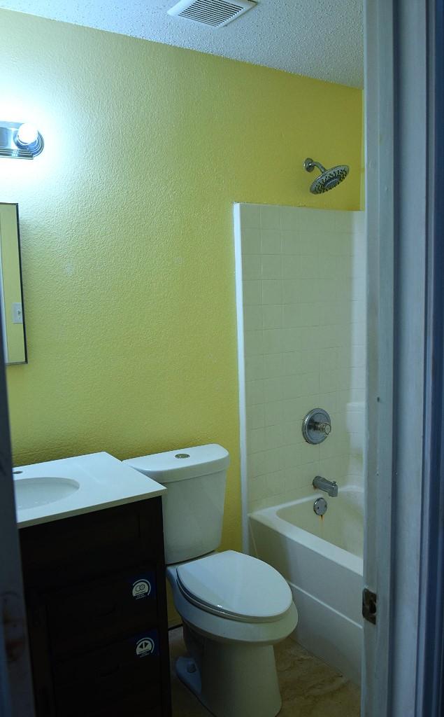 full bathroom featuring a textured ceiling, vanity, toilet, and  shower combination