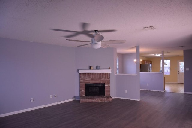 unfurnished living room with a textured ceiling, dark hardwood / wood-style floors, ceiling fan with notable chandelier, and a brick fireplace