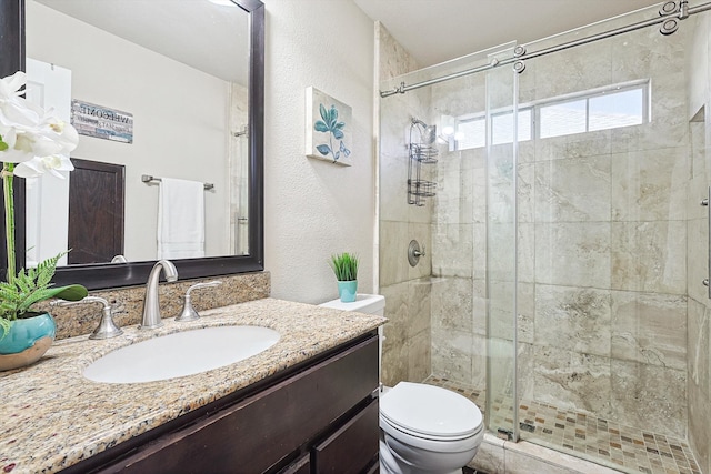 bathroom featuring a stall shower, toilet, vanity, and a textured wall