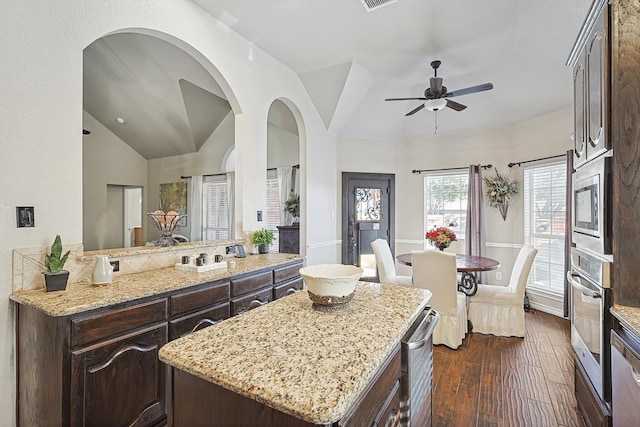 kitchen featuring light stone countertops, dark wood-style floors, lofted ceiling, dark brown cabinets, and appliances with stainless steel finishes