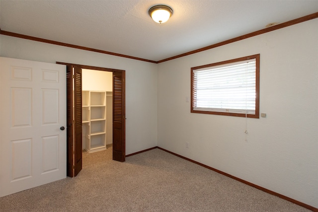 unfurnished bedroom with light carpet, a walk in closet, ornamental molding, a textured ceiling, and a closet