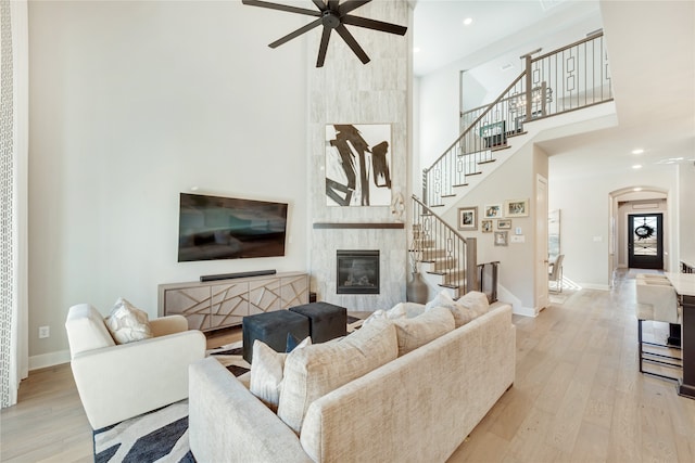 living room featuring ceiling fan, light hardwood / wood-style flooring, a tiled fireplace, and a high ceiling