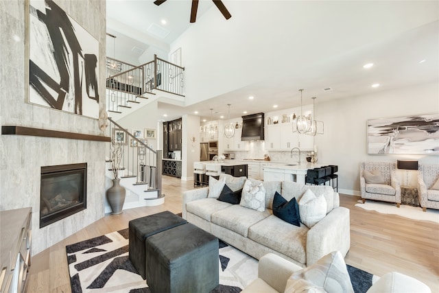 living room with a high ceiling, a fireplace, ceiling fan, and light wood-type flooring