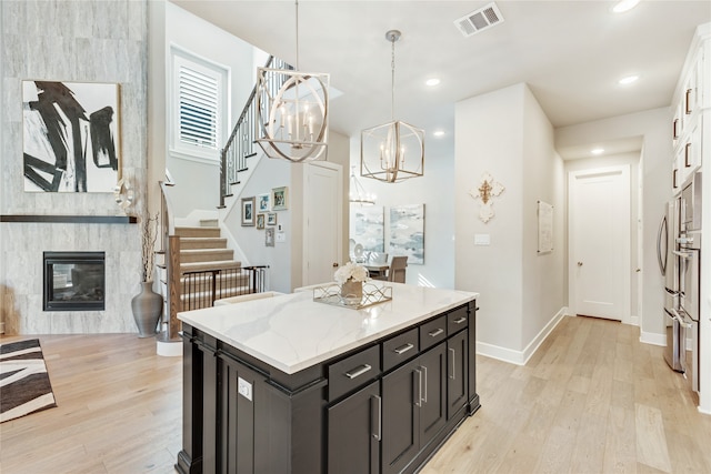 kitchen featuring a large fireplace, pendant lighting, a center island, light wood-type flooring, and white cabinetry