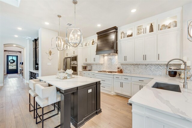 kitchen with appliances with stainless steel finishes, a center island, white cabinets, decorative light fixtures, and sink