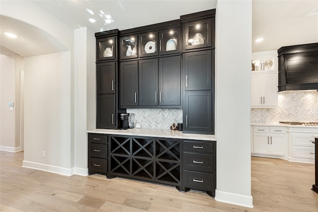 bar featuring white cabinets, stainless steel gas stovetop, light hardwood / wood-style flooring, and decorative backsplash