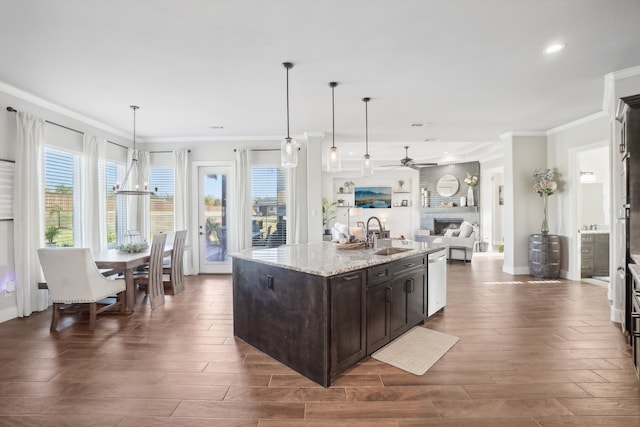 kitchen with light stone countertops, sink, dark hardwood / wood-style floors, an island with sink, and decorative light fixtures