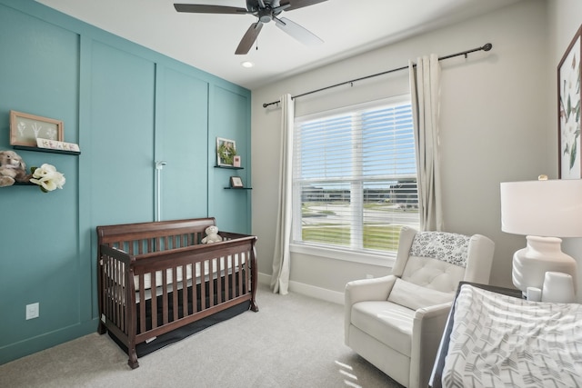 bedroom with multiple windows, light colored carpet, a nursery area, and ceiling fan