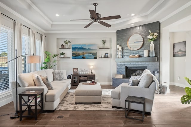 living room featuring ornamental molding, a raised ceiling, ceiling fan, a fireplace, and dark hardwood / wood-style floors