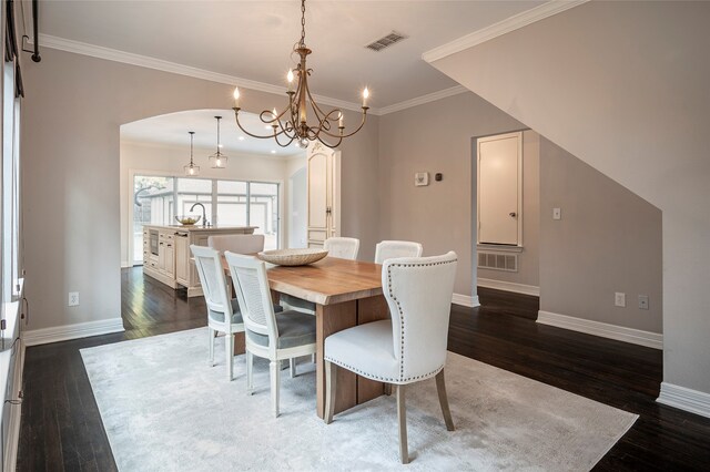 dining space featuring dark wood-type flooring, crown molding, sink, and a chandelier