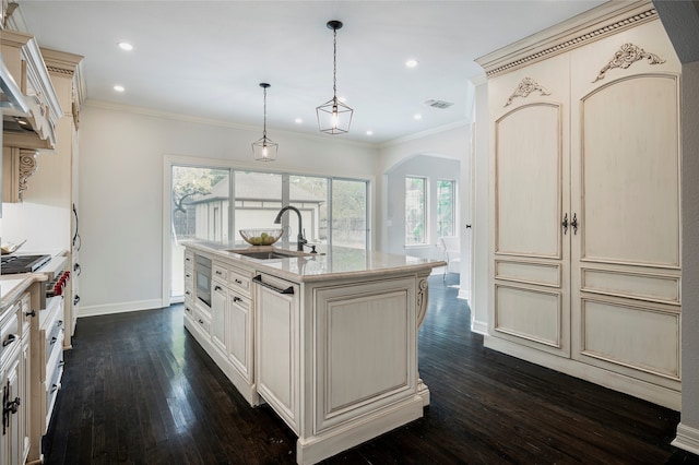 kitchen featuring sink, cream cabinetry, dark hardwood / wood-style flooring, pendant lighting, and a center island with sink