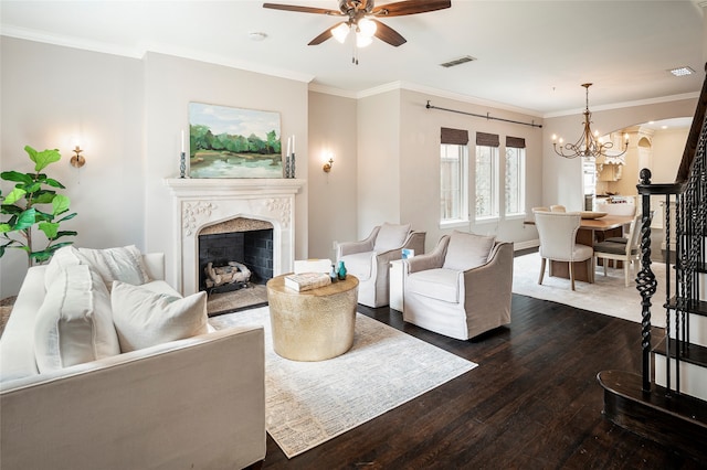 living room featuring dark wood-type flooring, crown molding, a fireplace, and ceiling fan with notable chandelier