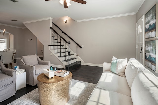 living room with dark wood-type flooring, ornamental molding, and ceiling fan with notable chandelier