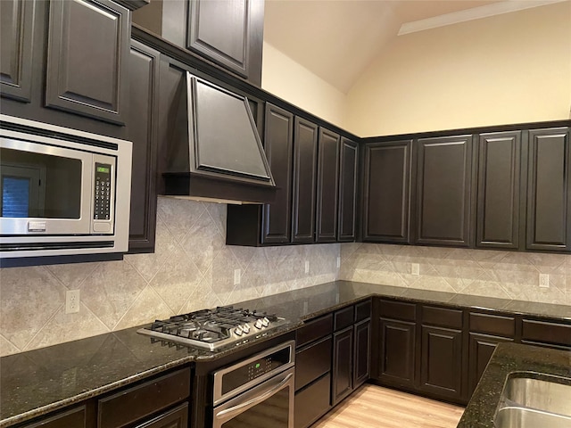 kitchen featuring custom exhaust hood, tasteful backsplash, appliances with stainless steel finishes, vaulted ceiling, and dark stone countertops