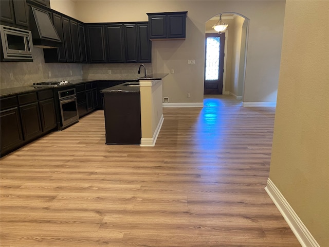 kitchen with stainless steel appliances, backsplash, sink, light wood-type flooring, and custom exhaust hood