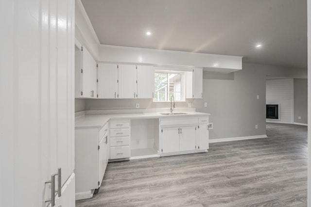 kitchen featuring a large fireplace, light hardwood / wood-style floors, white cabinets, and sink