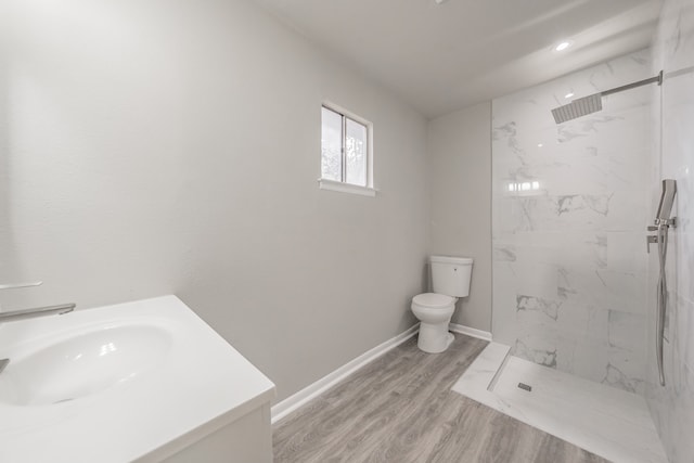 bathroom with hardwood / wood-style floors, toilet, vanity, and a tile shower