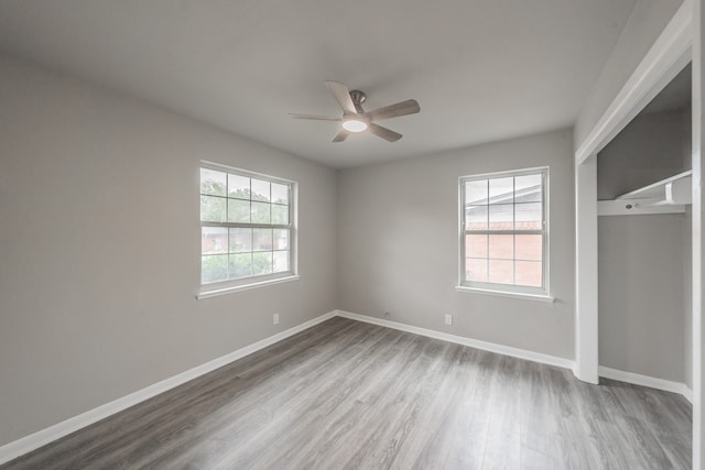 unfurnished bedroom featuring ceiling fan, multiple windows, hardwood / wood-style flooring, and a closet