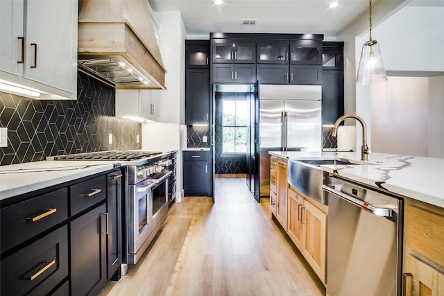 kitchen with light stone countertops, hanging light fixtures, light hardwood / wood-style floors, custom exhaust hood, and high end appliances