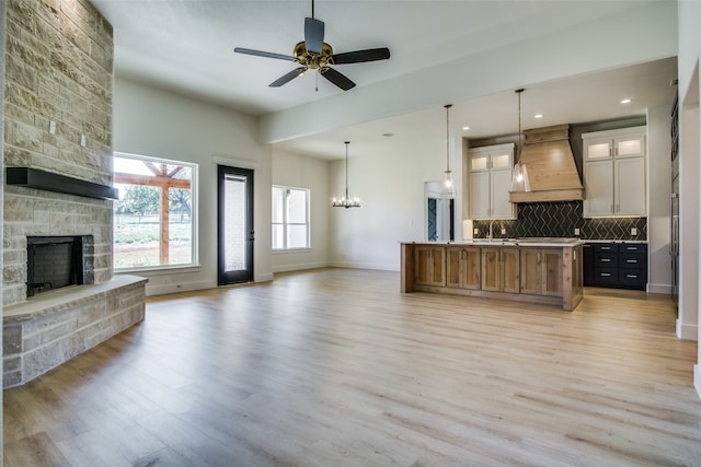 kitchen featuring a spacious island, a stone fireplace, backsplash, light wood-type flooring, and premium range hood