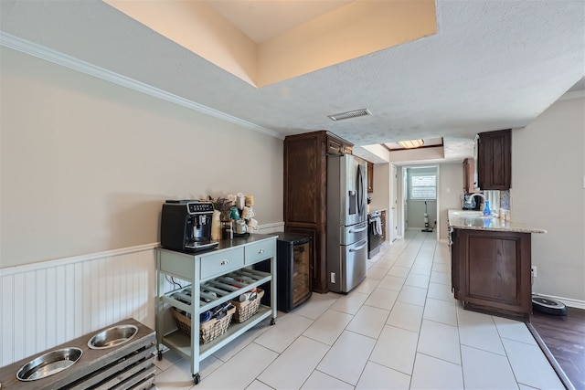 kitchen with appliances with stainless steel finishes, light tile patterned flooring, a textured ceiling, and dark brown cabinetry