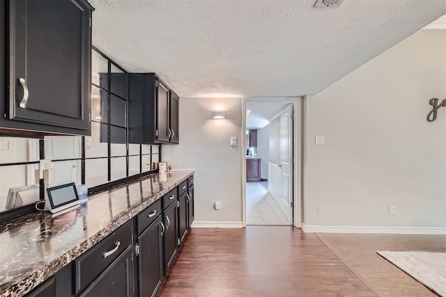 kitchen with a textured ceiling, dark hardwood / wood-style flooring, and dark stone countertops