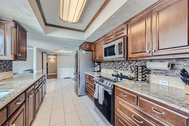 kitchen with a tray ceiling, stainless steel appliances, light stone counters, light tile patterned floors, and crown molding