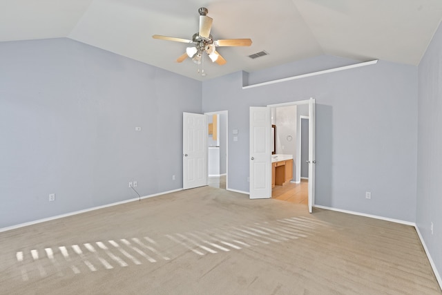 unfurnished bedroom featuring ceiling fan, ensuite bath, vaulted ceiling, and light colored carpet