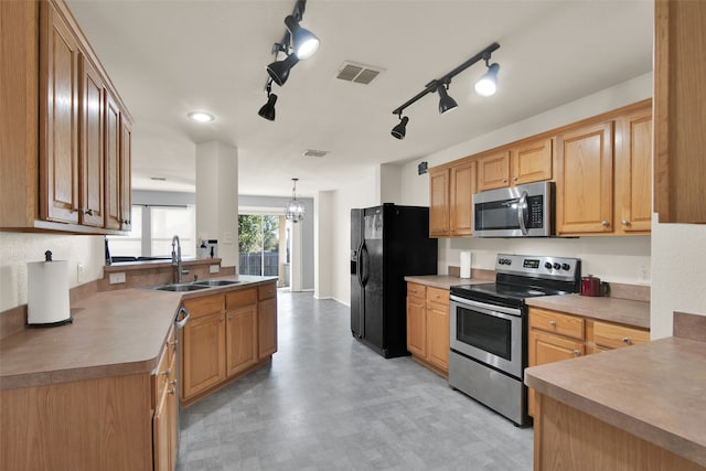 kitchen featuring stainless steel appliances, decorative light fixtures, sink, rail lighting, and a chandelier